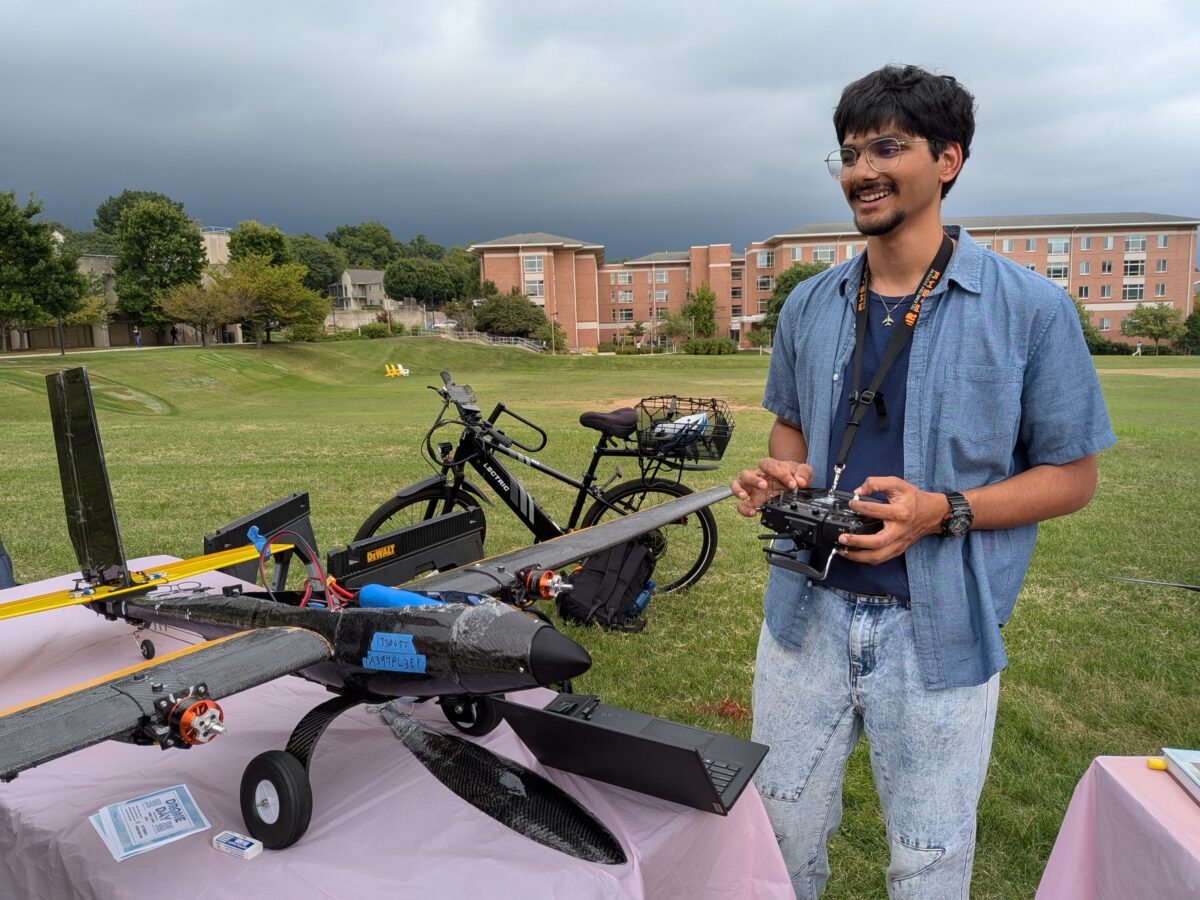 Student stands next to a small black plane that flies, navigates, and makes independent in-flight decisions without needing real-time control or intervention from a human pilot