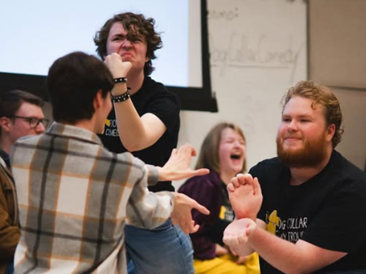 Five college students stand facing each other with their arms stretched out practicing improve comedy club
