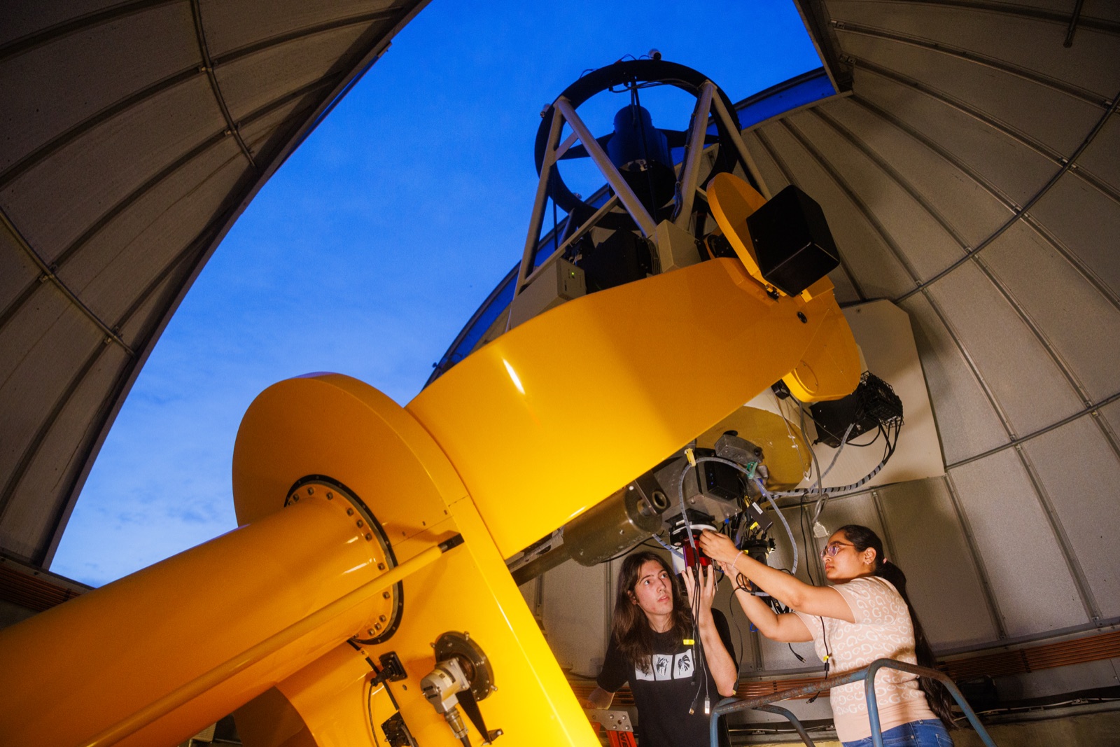 Students adjust the large yellow telescope inside the UMBC observatory dome