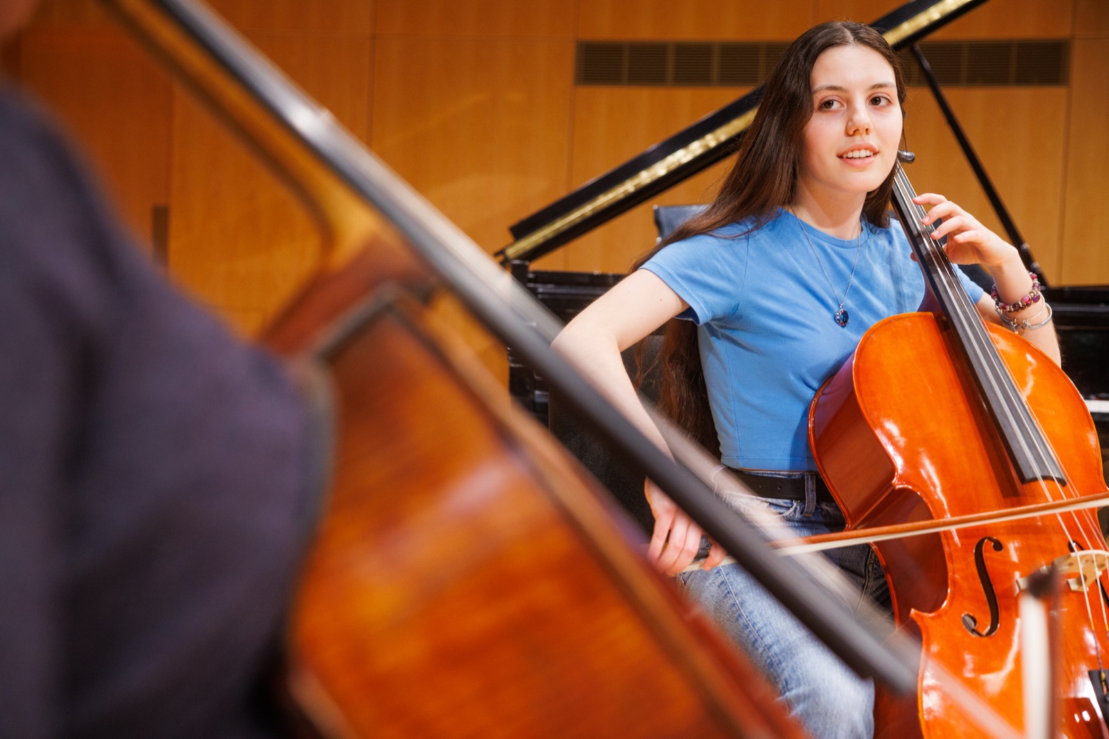 A student smiles while playing the cello during a rehearsal in a UMBC performance hall