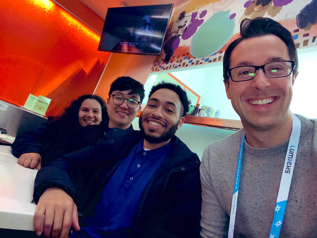 group photo of four people indoors, one wearing a conference lanyard around his neck
